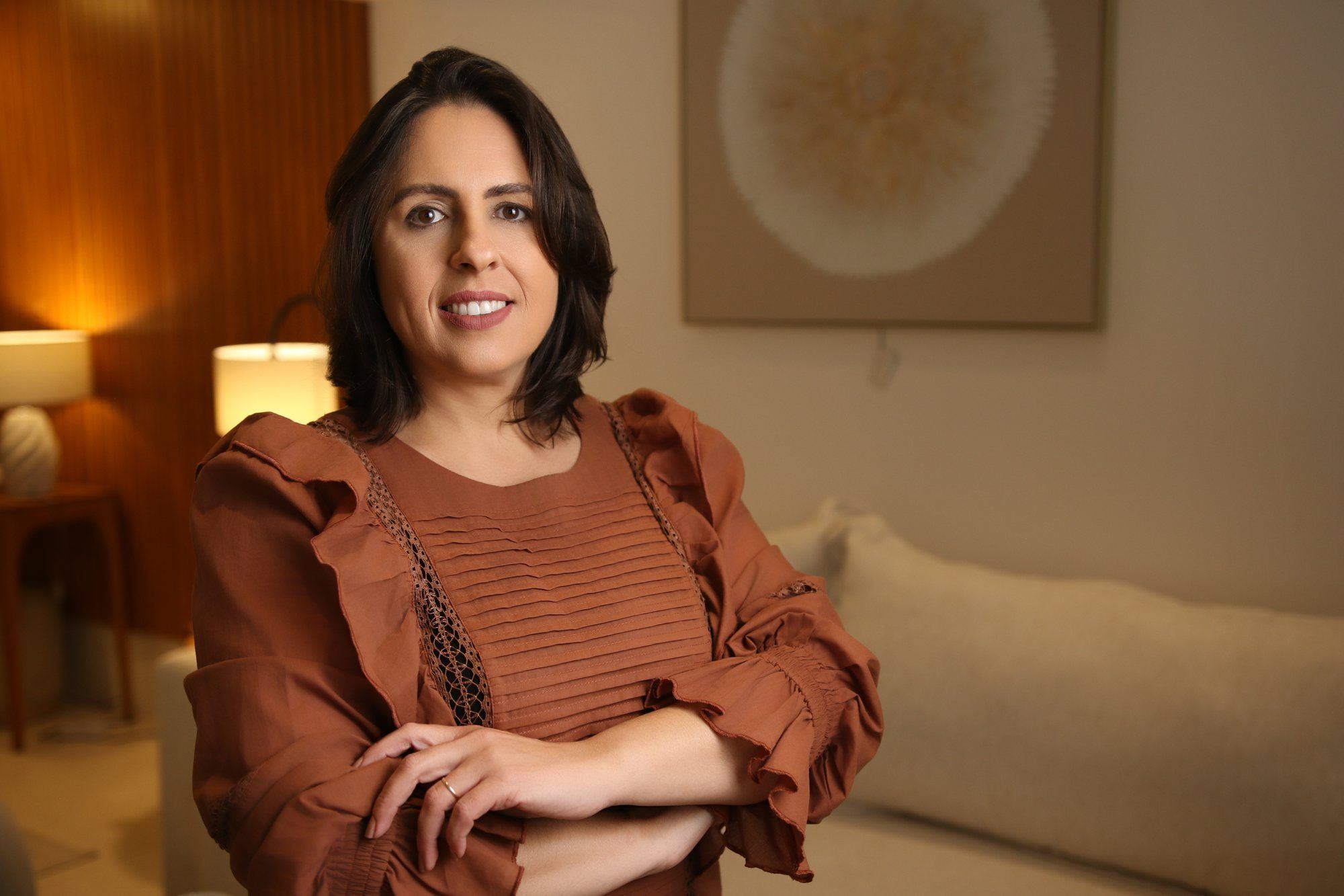 Roberta Borges, fundadora da EFCE, de braços cruzados e sorrindo, numa sala com luz quente de abajur.